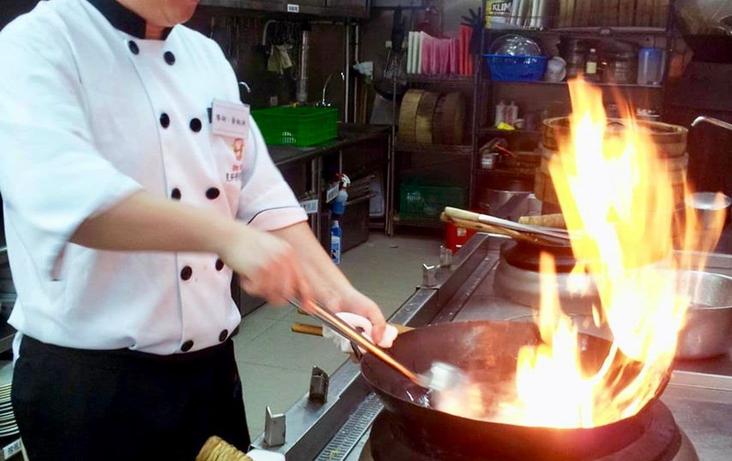 A chef stirring a flaming wok in a professional kitchen